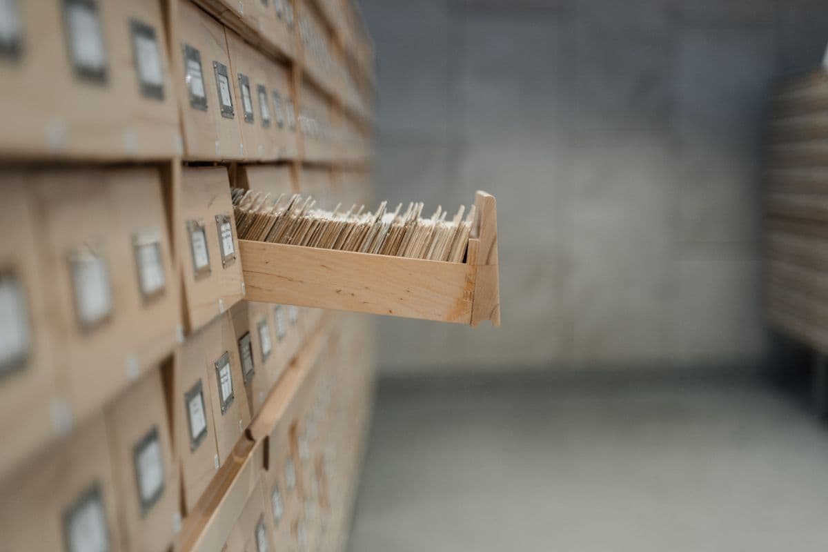 A wooden library card catalogue with one drawer pulled open, its index cards packed upright
