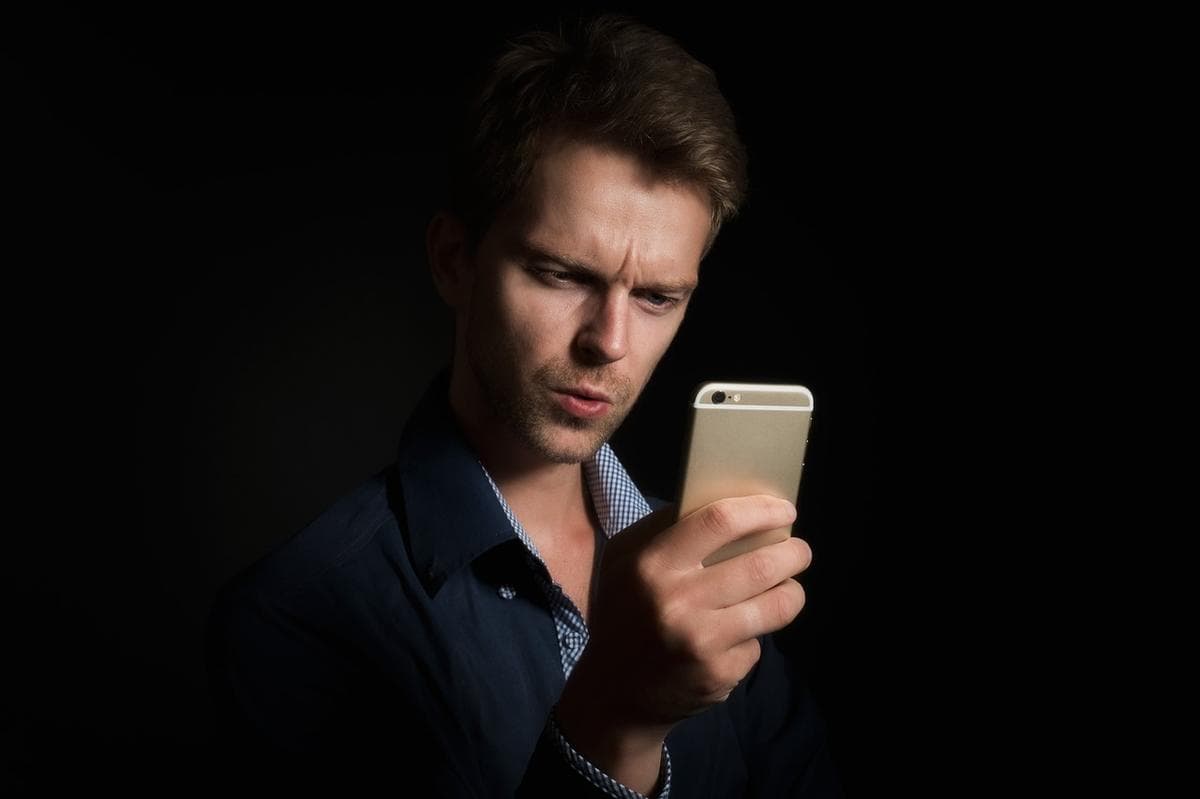 Um homem a olhar atentamente para o ecrã de um smartphone contra um fundo escuro