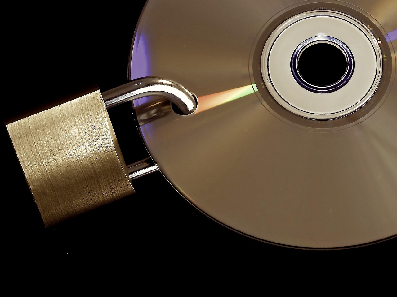 Un candado de latón apoyado sobre la superficie de un disco óptico contra un fondo negro